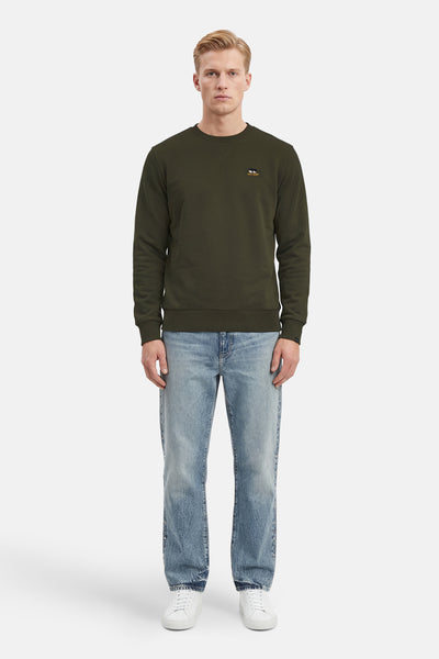 Kaki sweatshirt van ANTWRP, met geborduurd logo, gedragen met een lichtblauwe jeans en witte sneakers.