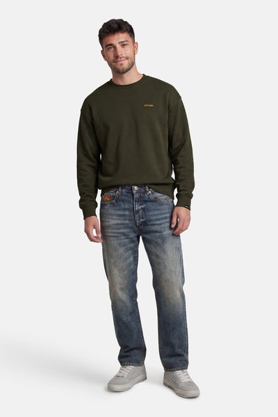 Sweat-shirt kaki à col rond de ANTWRP, porté avec un jean bleu délavé et des baskets grises.
