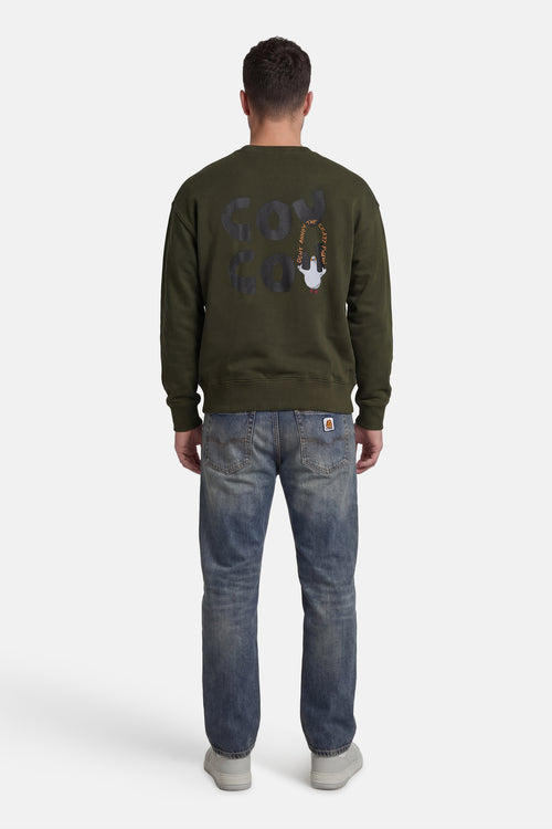 Kaki ANTWRP sweatshirt met print op de rug, gedragen met een blauwe jeans en grijze sneakers.