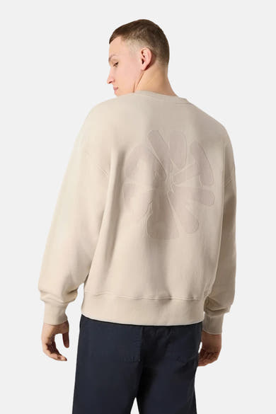 Sweat-shirt écru de ANTWRP, avec un motif ton sur ton dans le dos, porté avec un pantalon bleu marine.
