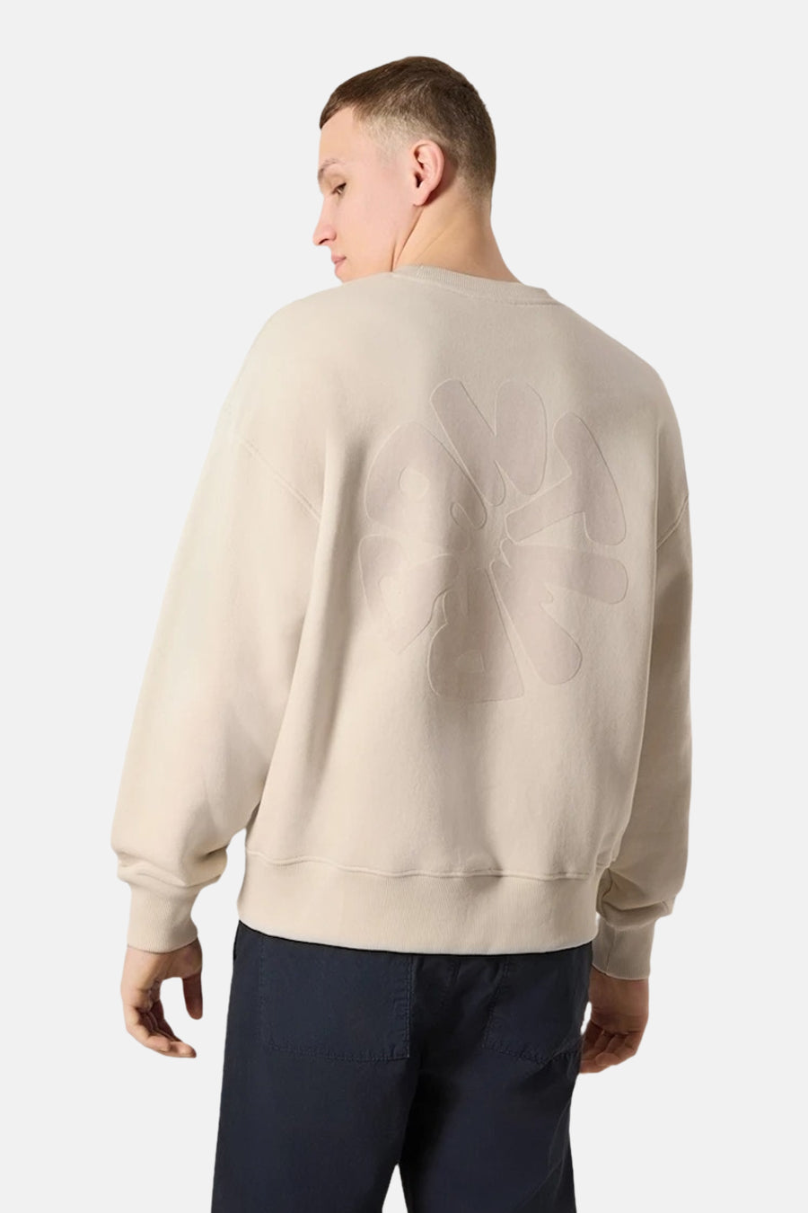Sweat-shirt écru de ANTWRP, avec un motif ton sur ton dans le dos, porté avec un pantalon bleu marine.
