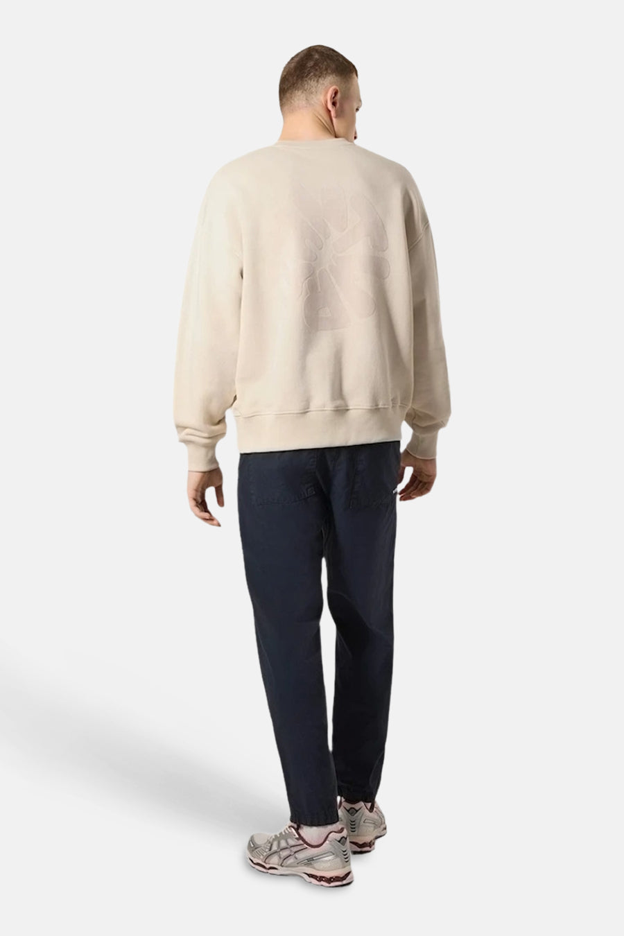 Sweat-shirt écru de ANTWRP, avec un motif ton sur ton dans le dos, porté avec un pantalon bleu marine.