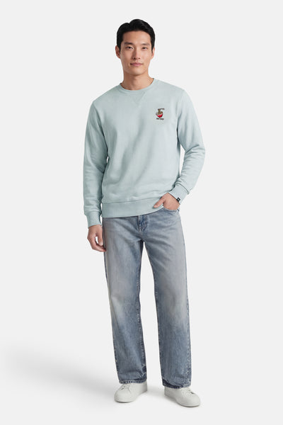 Sweat-shirt bleu, de ANTWRP, avec un motif brodé sur la poitrine, porté avec un jean et des baskets blanches.
