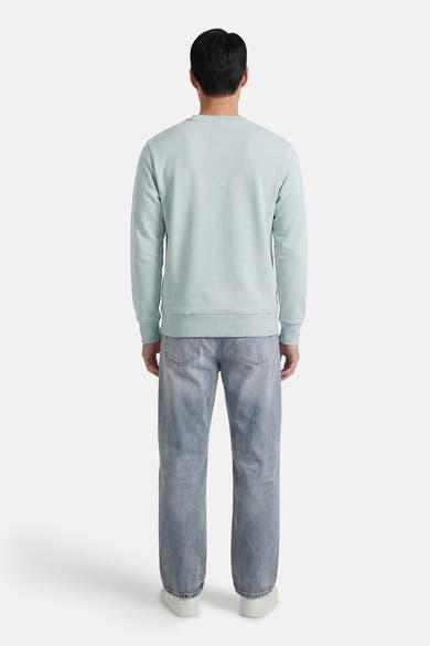 Sweat-shirt bleu col rond de ANTWRP, porté avec un jean délavé et des chaussures de sport blanches, vue de dos.
