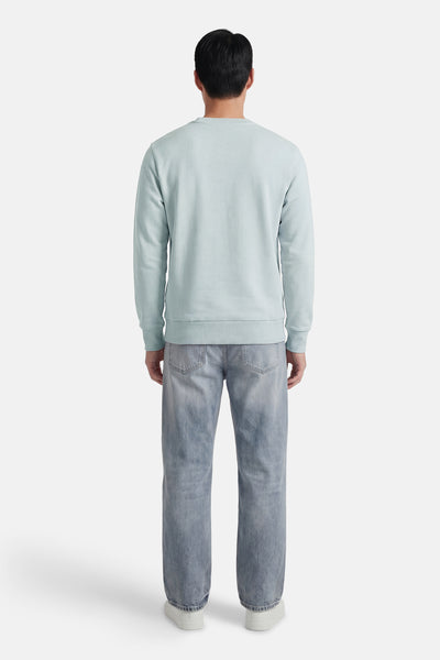 Sweat-shirt bleu col rond de ANTWRP, porté avec un jean délavé et des chaussures de sport blanches, vue de dos.
