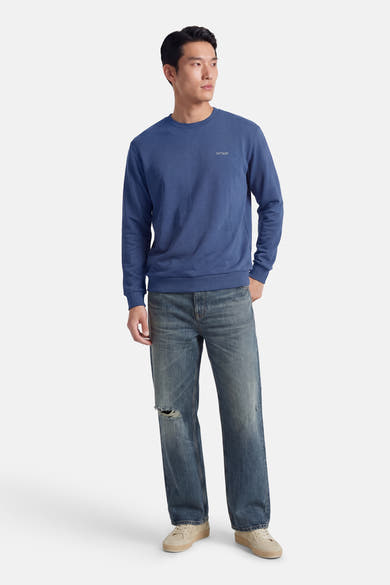Sweat-shirt bleu col rond de ANTWRP, porté avec un jean délavé troué et des baskets beige.