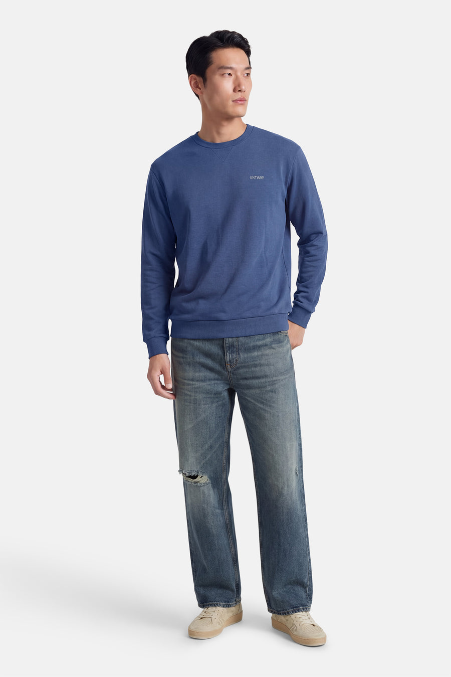 Sweat-shirt bleu col rond de ANTWRP, porté avec un jean délavé troué et des baskets beige.