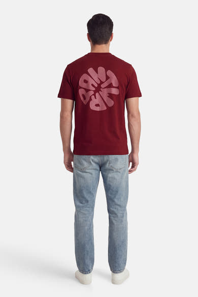T-shirt à manches courtes rose, par ANTWRP, avec motif graphique au dos, porté avec un jean et des chaussures blanches.