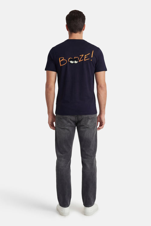 T-shirt à manches courtes bleu marine de ANTWRP avec inscription humoristique orange au dos, porté avec un jean gris.
