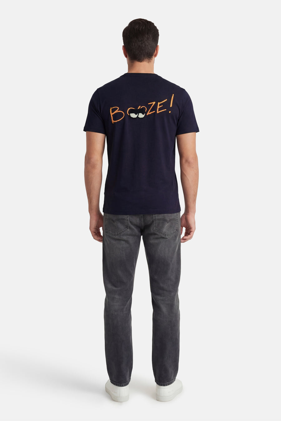 Marineblauwe T-shirt met korte mouwen van ANTWRP met oranje humoristische opdruk op de rug, gedragen met een grijze jeans.