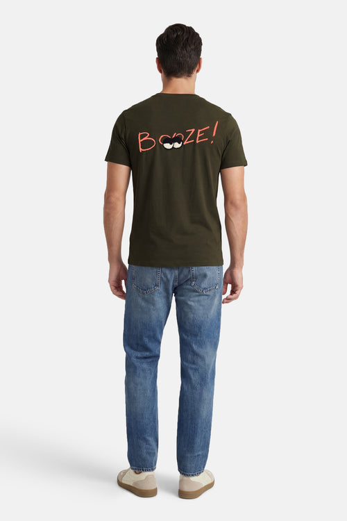 T-shirt kaki à manches courtes de ANTWRP avec inscription humoristique sur le dos, porté avec un jean bleu.

