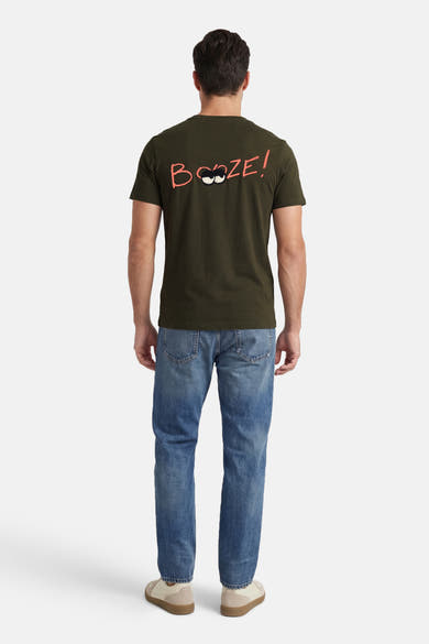 T-shirt kaki à manches courtes de ANTWRP avec inscription humoristique sur le dos, porté avec un jean bleu.
