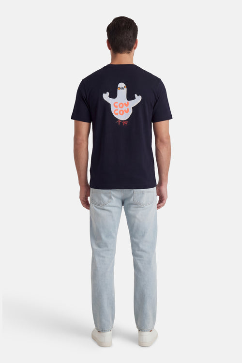 T-shirt à manches courtes bleu de ANTWRP, avec un imprimé de pigeon et porté avec un jean clair et des chaussures blanches.