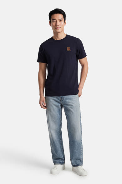 T-shirt à manches courtes bleu d'ANTWRP, avec un patch logo sur la poitrine, porté avec un jean délavé et des baskets blanches.
