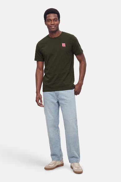 T-shirt à manches courtes kaki de ANTWRP, avec un motif carré rose sur la poitrine, porté avec un jean bleu clair et des baskets beige.