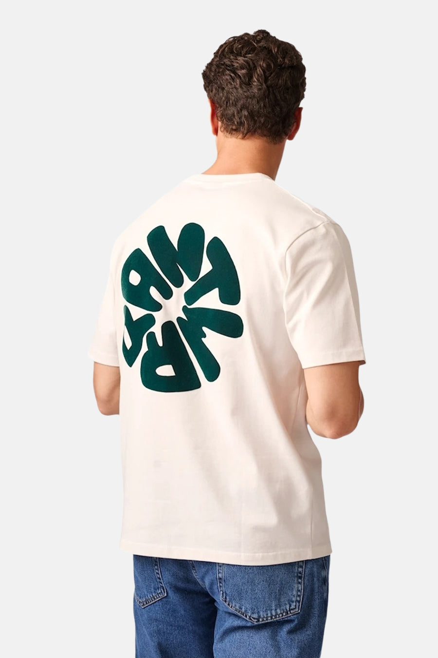 Ecru short-sleeve t-shirt with bold green circular graphic on back, worn by model in blue jeans, back view