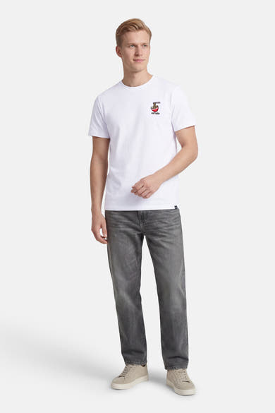 T-shirt blanc à manches courtes de ANTWRP, avec un motif brodé et porté avec un jean gris et des baskets beiges.
