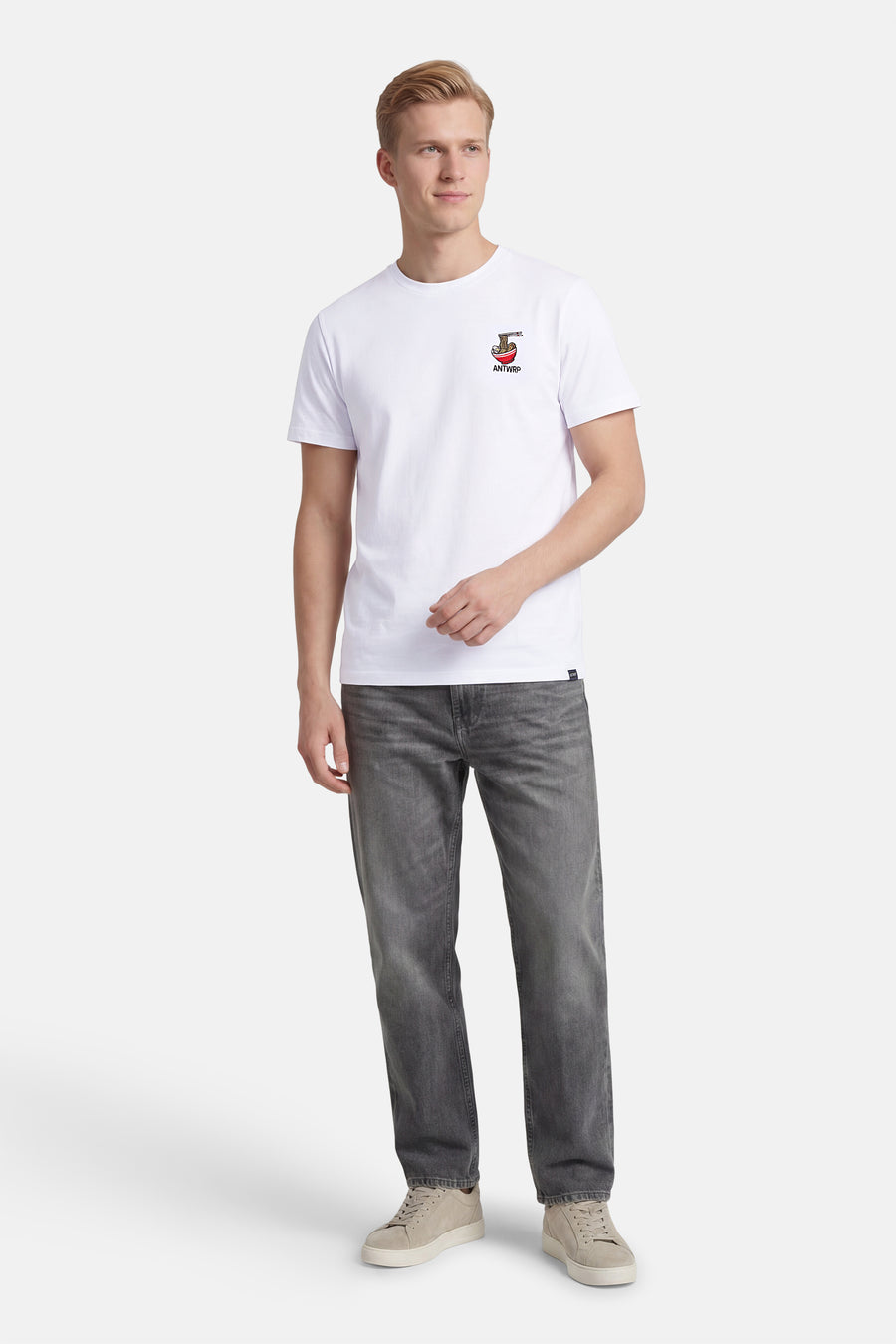 T-shirt blanc à manches courtes de ANTWRP, avec un motif brodé et porté avec un jean gris et des baskets beiges.

