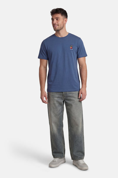 T-shirt à manches courtes bleu, par ANTWRP, avec un motif brodé discret et porté avec un jean décontracté et des chaussures de sport.