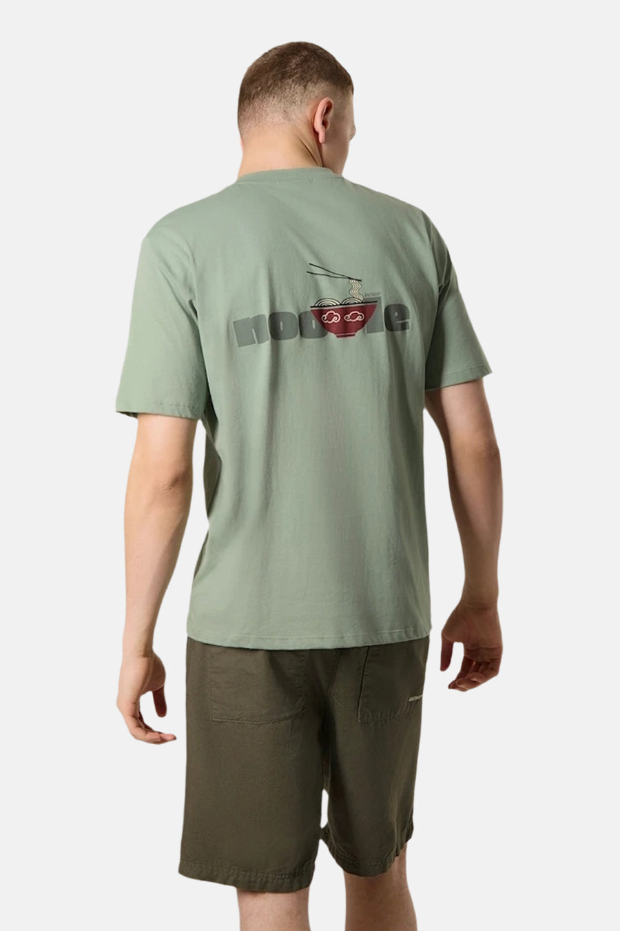 T-shirt à manches courtes vert d'ANTWRP, avec imprimé de nouilles au dos, porté avec un short kaki.
