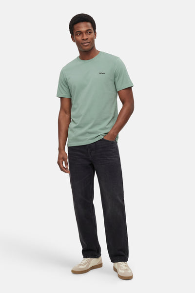 T-shirt à manches courtes vert de ANTWRP, porté avec un jean noir et des baskets beiges.