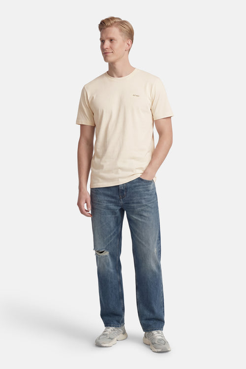 T-shirt à manches courtes écru de ANTWRP, porté avec un jean bleu délavé et des baskets grises.
