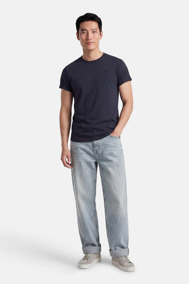 T-shirt à manches courtes bleu d'ANTWRP, avec des manches retroussées, porté avec un jean décontracté et des chaussures de sport.