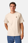 Ecru short-sleeve t-shirt with small embroidered bird design on chest, worn by model in front view with blue jeans