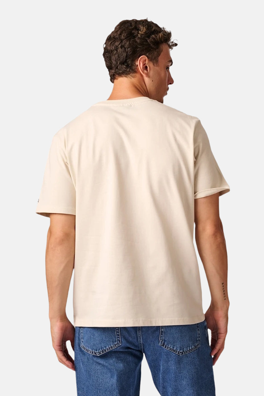 Ecru short-sleeve t-shirt from back view, plain cotton fabric, relaxed fit, worn with blue jeans