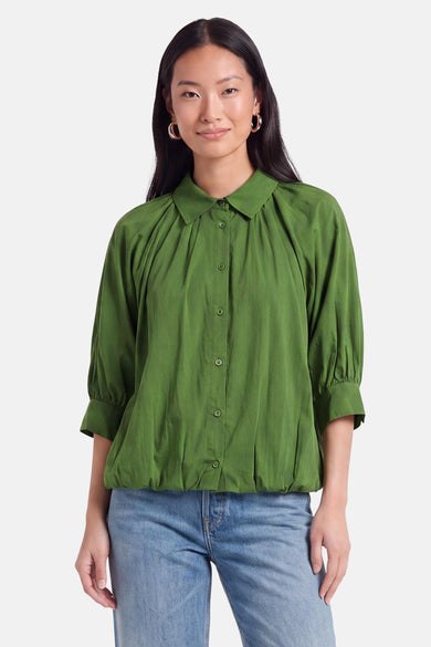 Chemise verte à manches courtes de style ample par AMELIE ET AMELIE, avec col boutonné et détails plissés au devant, portée avec un jean bleu clair.