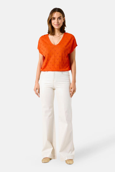 Pull à col en V orange de GARCIA, à motif ajouré, porté avec un jean blanc évasé et des chaussures plates dorées.