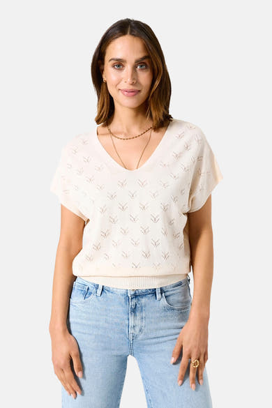 Ecru V-hals trui van GARCIA, met ajourpatroon, gedragen met een lichtblauwe jeans en gouden kettingen.