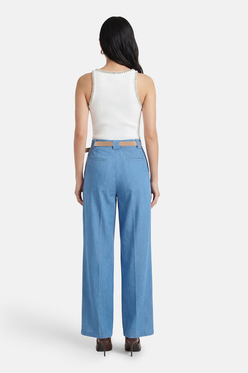 Pantalon de costume bleu clair en denim d'Amélie et Amélie, avec ceinture marron et chaussures à talons foncées.