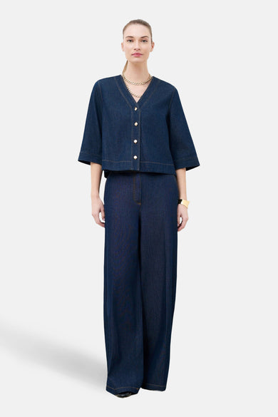 Chemise à manches courtes en denim bleu foncé de Caroll, avec boutons dorés et col en V, portée avec un pantalon assorti.