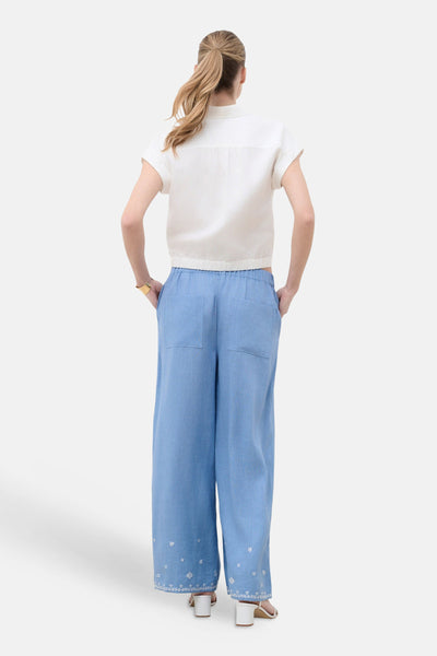 Chemise blanche à manches courtes de CAROLL, de dos avec ourlet élastique et pantalon large bleu brodé.