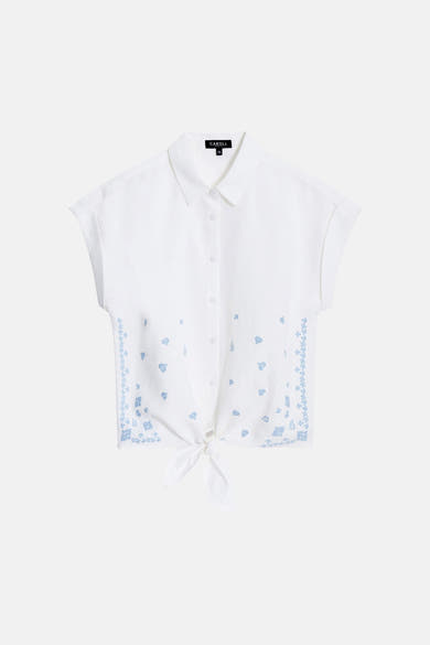 Chemise blanche de Caroll à manches courtes, nouée à la taille avec motifs floraux bleus.