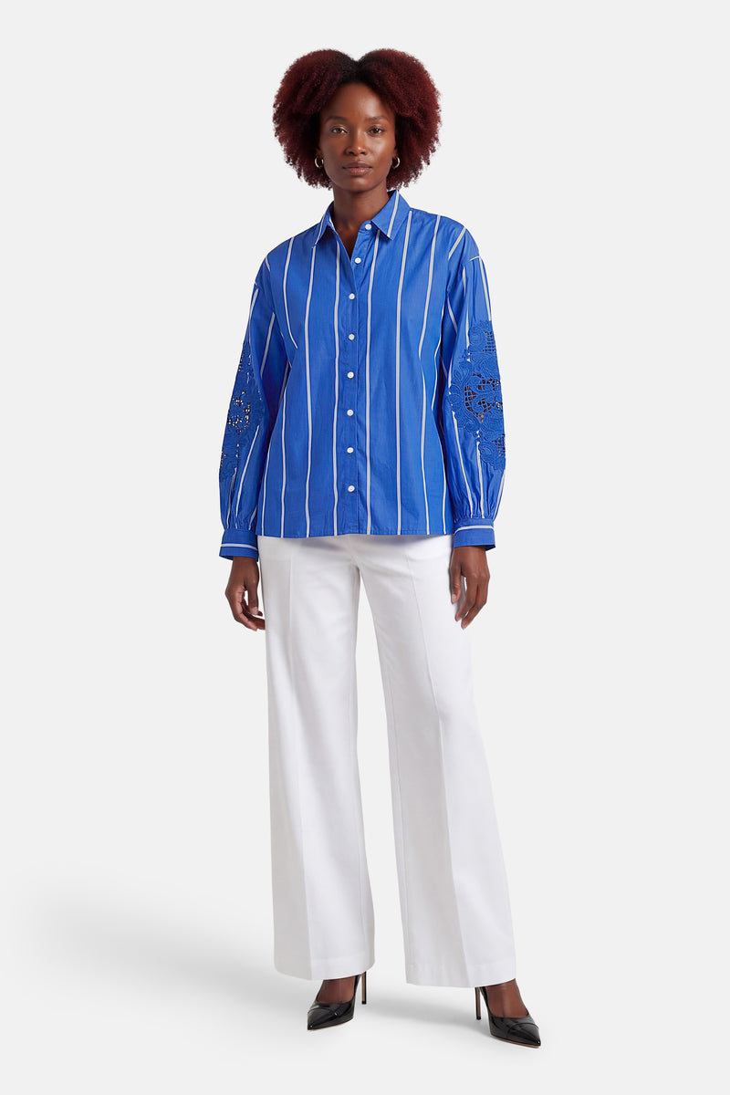 Blauw gestreept overhemd van CAROLL met lange mouwen versierd met ajourwerk, gedragen met een witte broek.