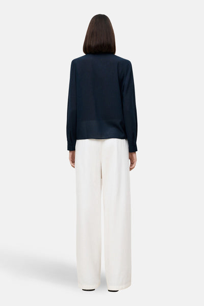 Chemise à manches longues bleue à carreaux par CAROLL, vue de dos avec un pantalon blanc à jambes larges.
