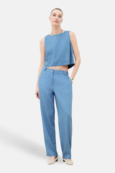 Mouwloos topje van lichtblauw denim van CAROLL, gedragen met een bijpassende broek en een gouden ketting.