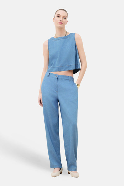 Mouwloos topje van lichtblauw denim van CAROLL, gedragen met een bijpassende broek en een gouden ketting.