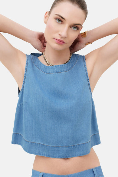 Mouwloos top van lichtblauw denim van CAROLL, met ronde hals en gouden ketting, gedragen met een gouden armband.