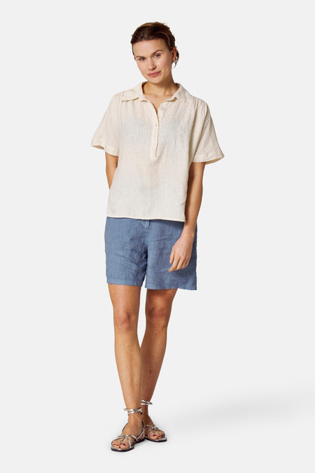 Ecru blouse met korte mouwen van COPINES D'ANVERS, met knoopsluiting, gedragen met een blauwe short en zilveren sandalen.