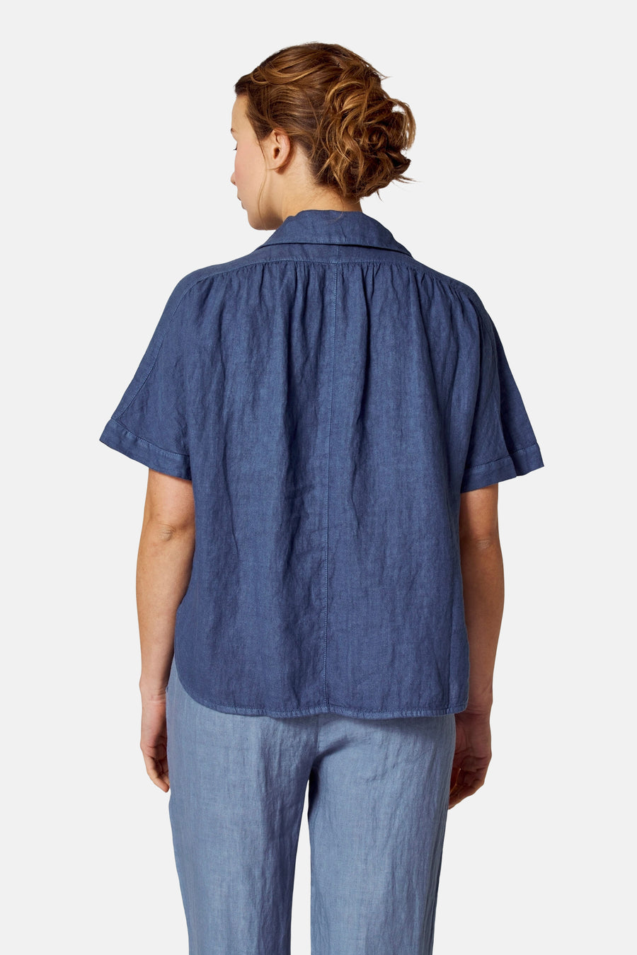 Blauwe blouse met korte mouwen van COPINES D'ANVERS, met plooien aan de achterkant, gedragen met een blauwe broek.