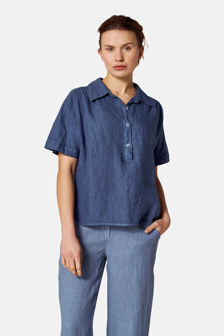 Blauwe blouse met korte mouwen van COPINES D'ANVERS, gedragen met een bijpassende broek, hand in de zak.