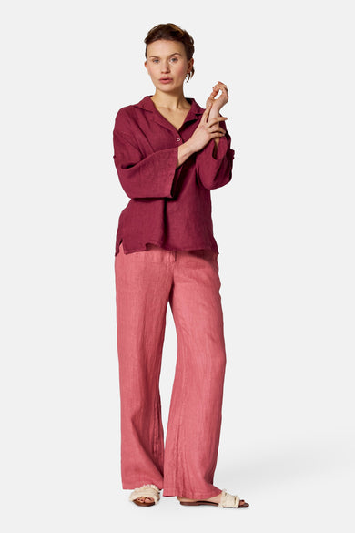 Chemisier bordeaux à manches longues de Copines d'Anvers, porté avec un pantalon rose ample et des sandales à franges.
