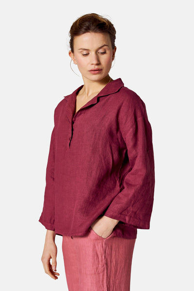 Chemisier bordeaux en lin de COPINES D'ANVERS, à col classique et manches trois-quarts amples, porté avec un pantalon rose.