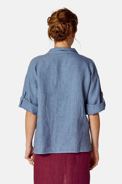 Blauwe blouse (korte mouwen) van COPINES D'ANVERS met opgerolde mouwen en linnen textuur, gedragen met een bordeauxrode rok.