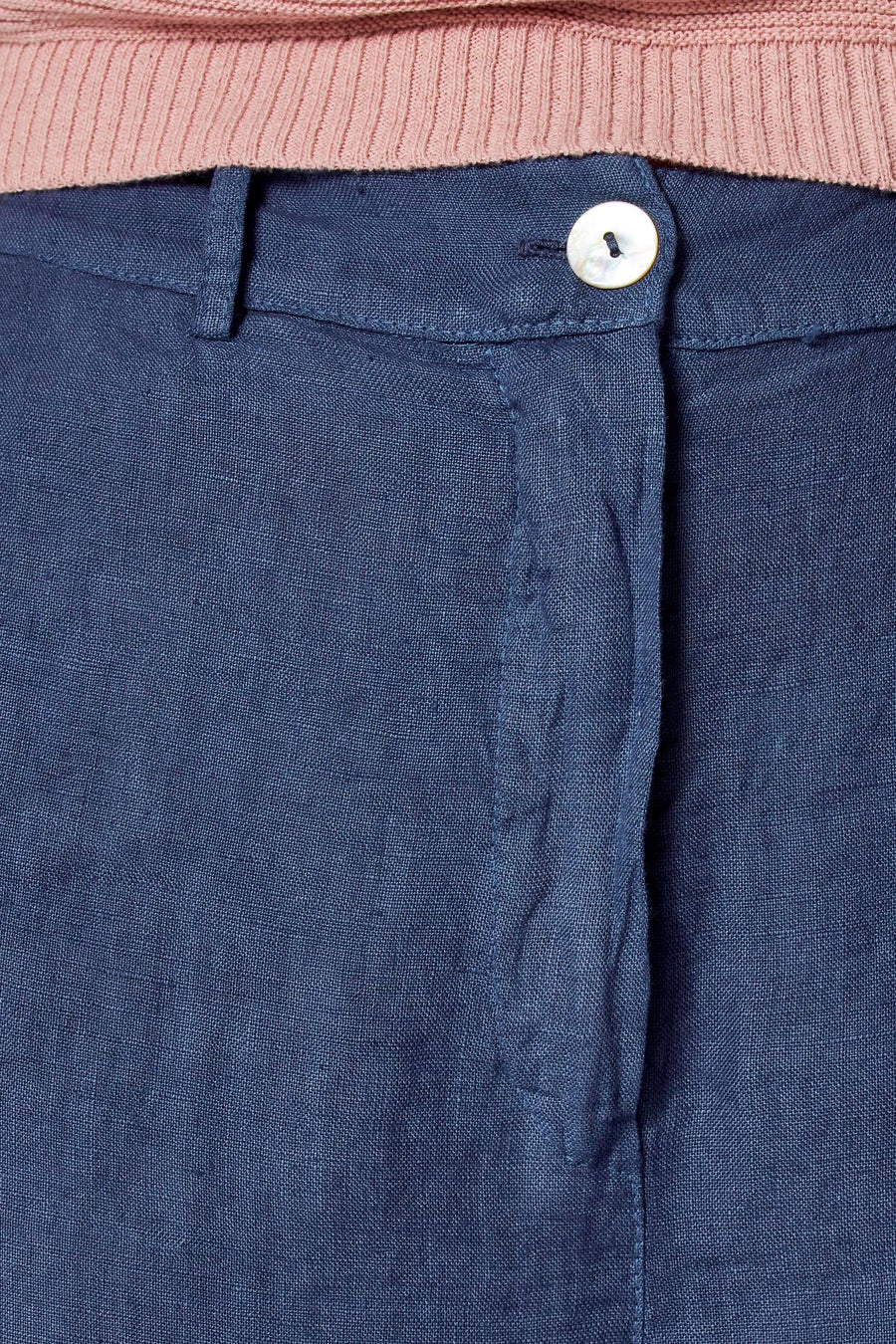Gekleurde blauwe linnen broek van COPINES D'ANVERS, met parelmoeren knoopsluiting, onder een roze trui.