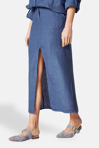 Jupe longue bleu en lin de COPINES D'ANVERS avec fente, portée avec des chaussures à motif zébré.