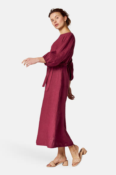 Robe bordeaux de COPINES D'ANVERS avec une ceinture nouée et des chaussures nude à talons.